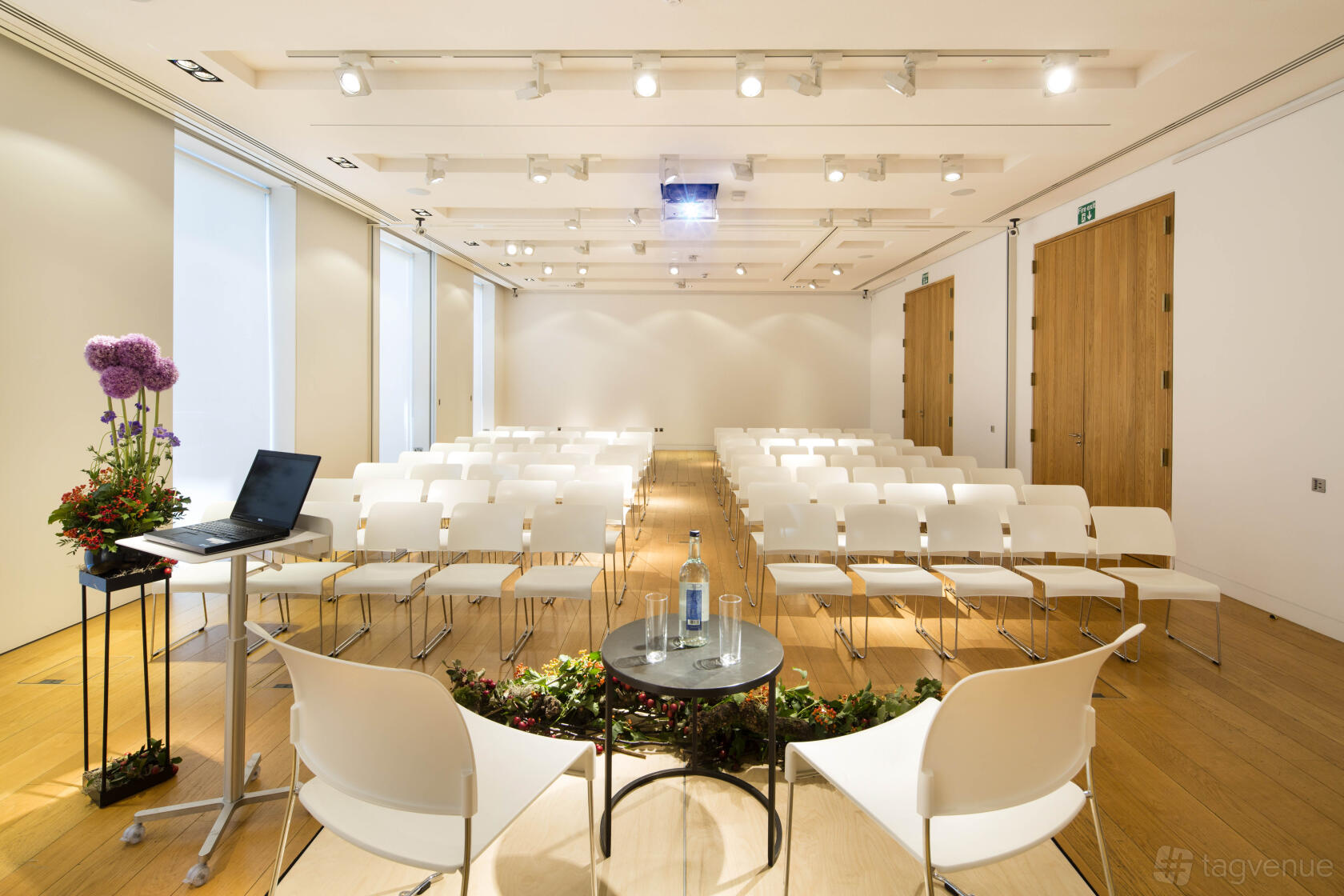 An event space with rows of white chairs, wooden floors, and a projector screen at The Goldsmiths' Centre.