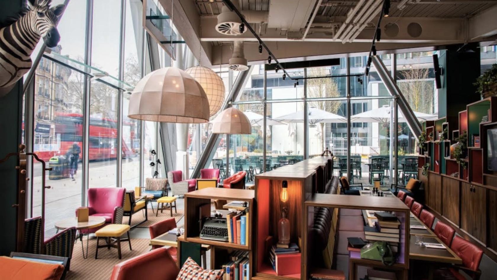 A bar in a pub with floor-to-ceiling windows, colorful armchairs, and bookshelves at Greenwood.