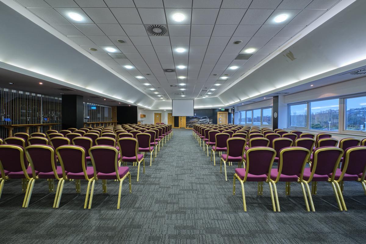 An auditorium with rows of cushioned chairs facing a projector screen and floor-to-ceiling windows at Swansea.com Stadium.