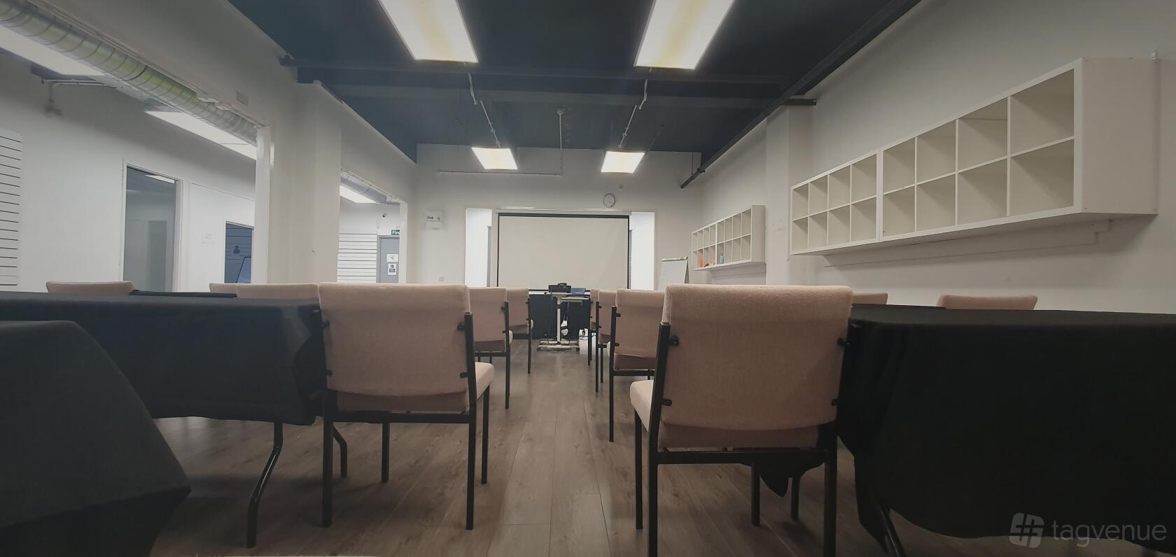 An auditorium with rows of upholstered chairs, a projector screen, and ceiling strip lighting at Glasgow Rooms.