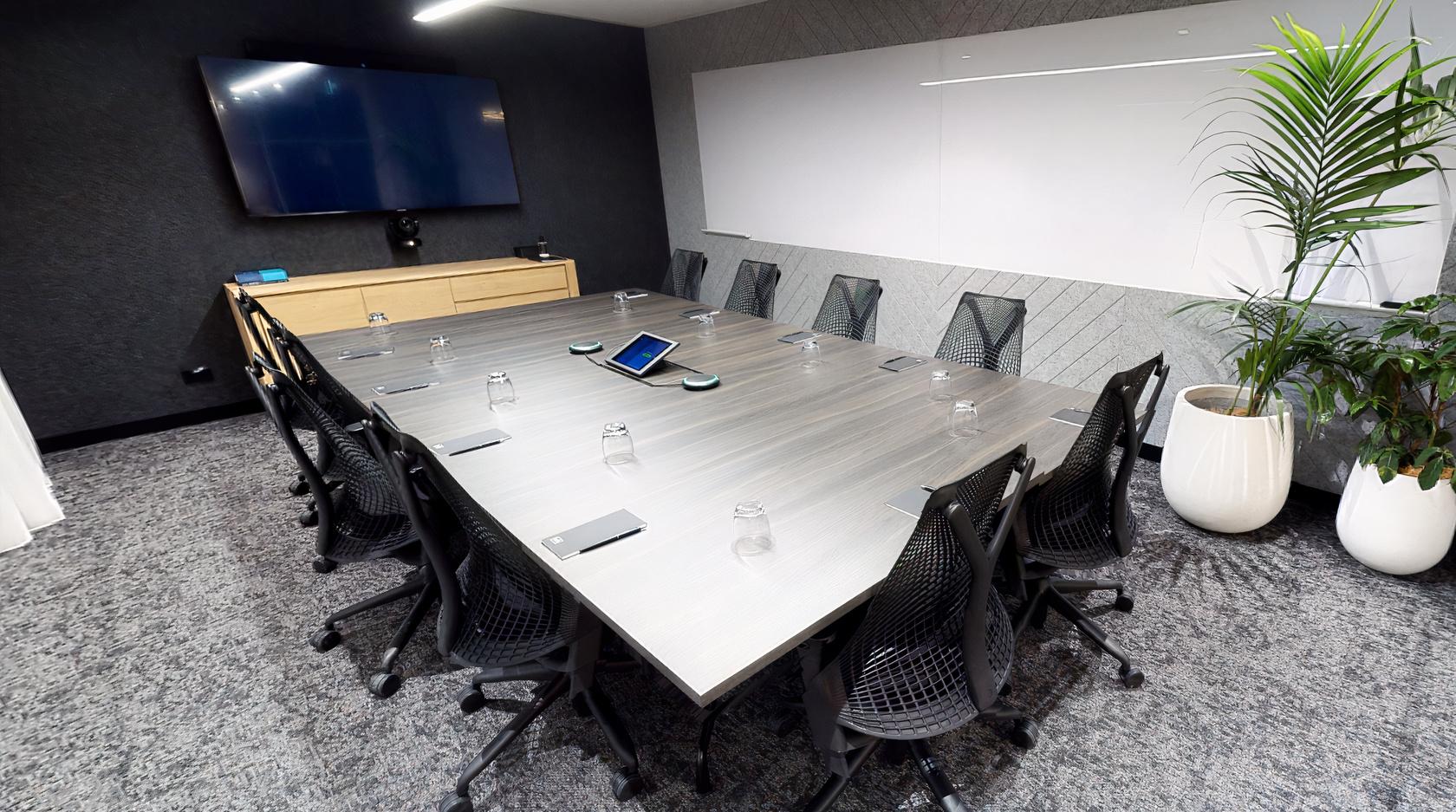 A coworking space with a large conference table, mesh chairs, a wall-mounted screen, and a whiteboard at Hub St Kilda Road.