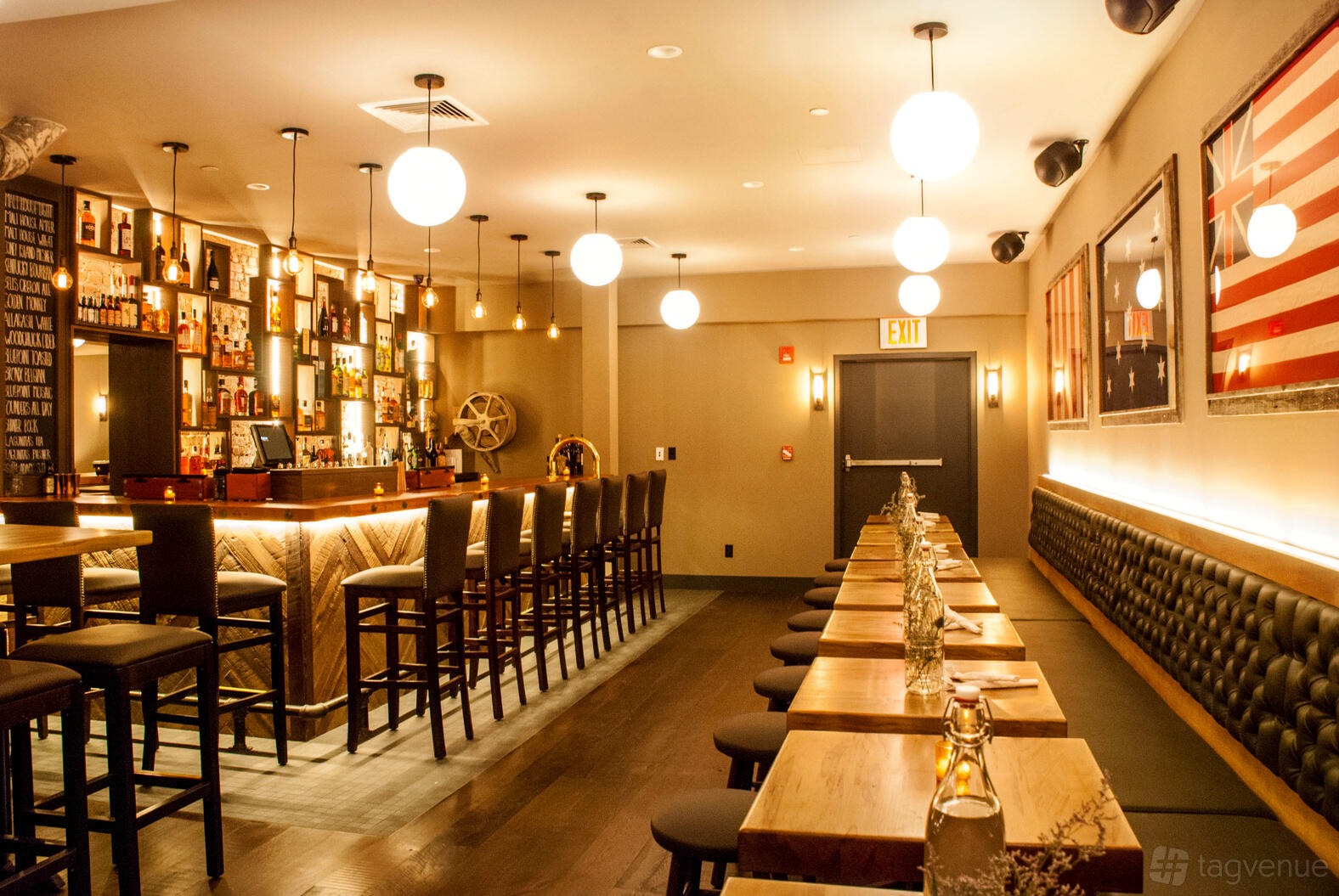 A restaurant bar with globe pendant lighting, a long banquette, and wood tables at The Malthouse Financial District.