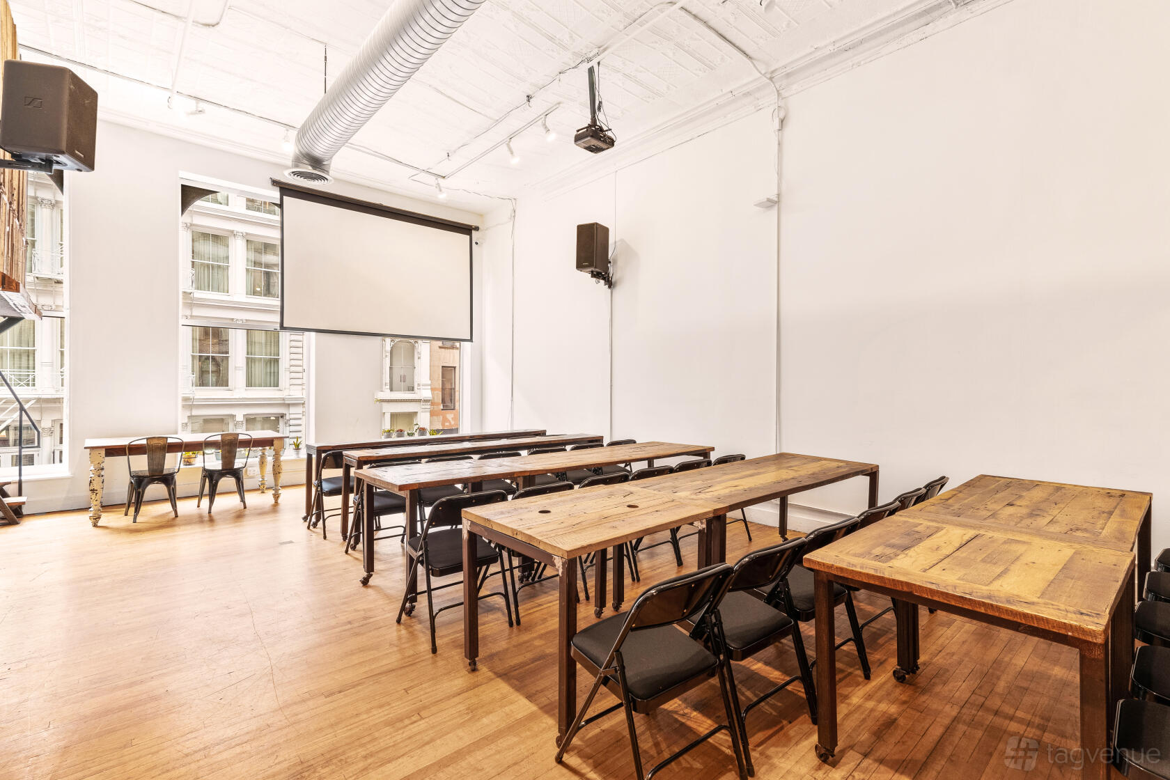 A function room with natural light, exposed ductwork, and wooden tables with folding chairs at The Farm Soho.