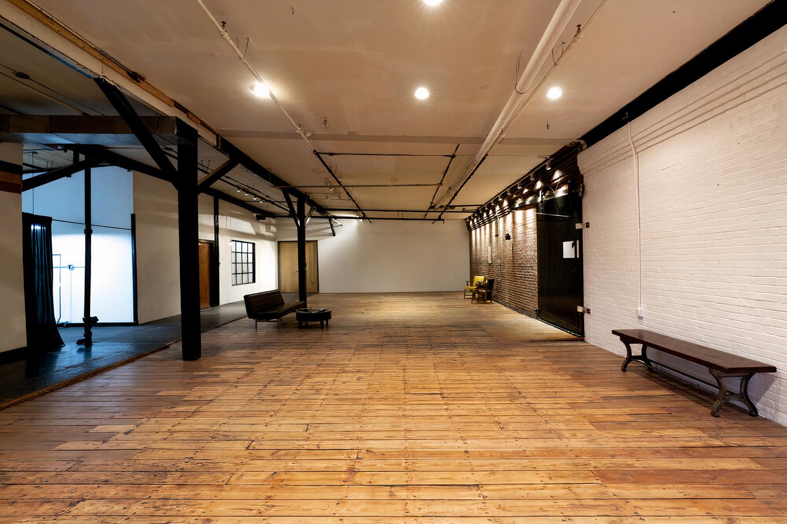 An event space with wide wooden floors, exposed beams, and a mix of brick and white walls at Ambient + Studio.