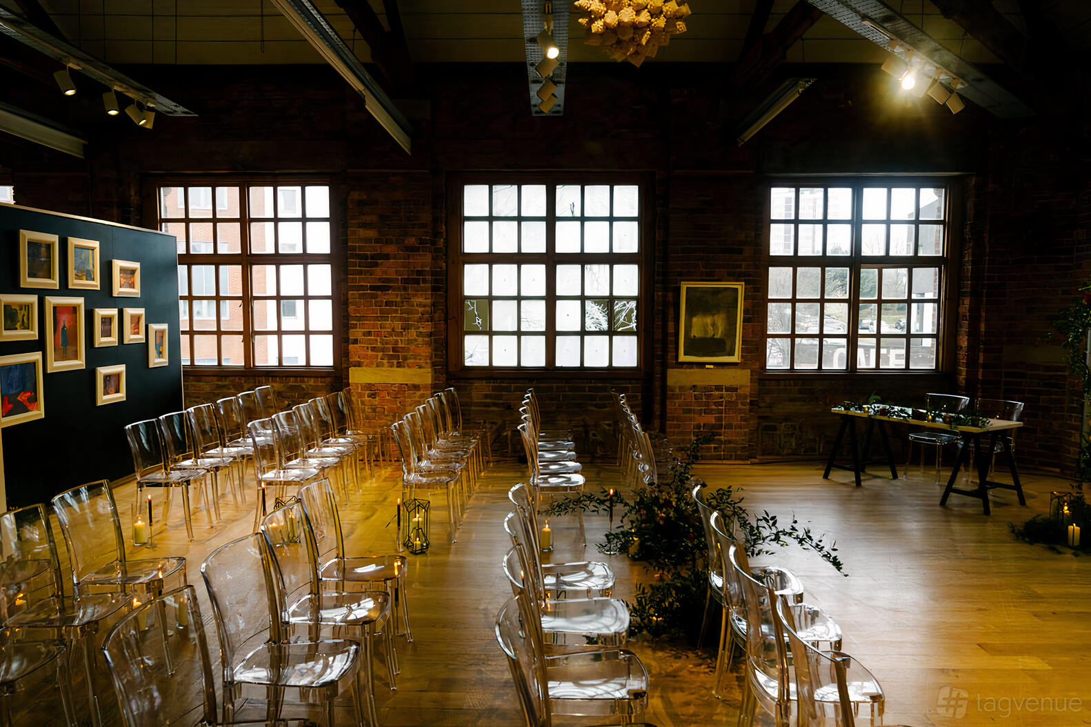 An event venue with exposed brick walls, large industrial windows, and clear chairs arranged in rows at The Biscuit Factory.