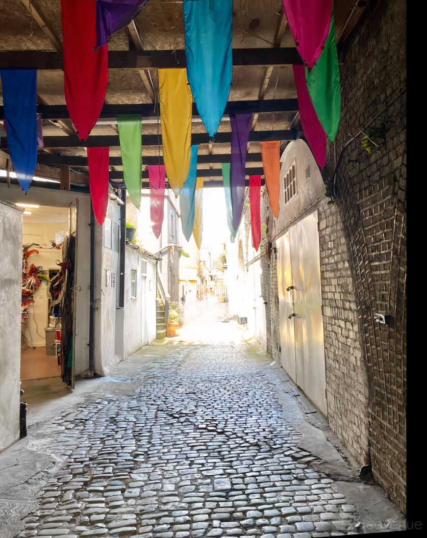 A cobblestone passageway with colorful hanging flags under a wooden ceiling at Sunshine International Arts.