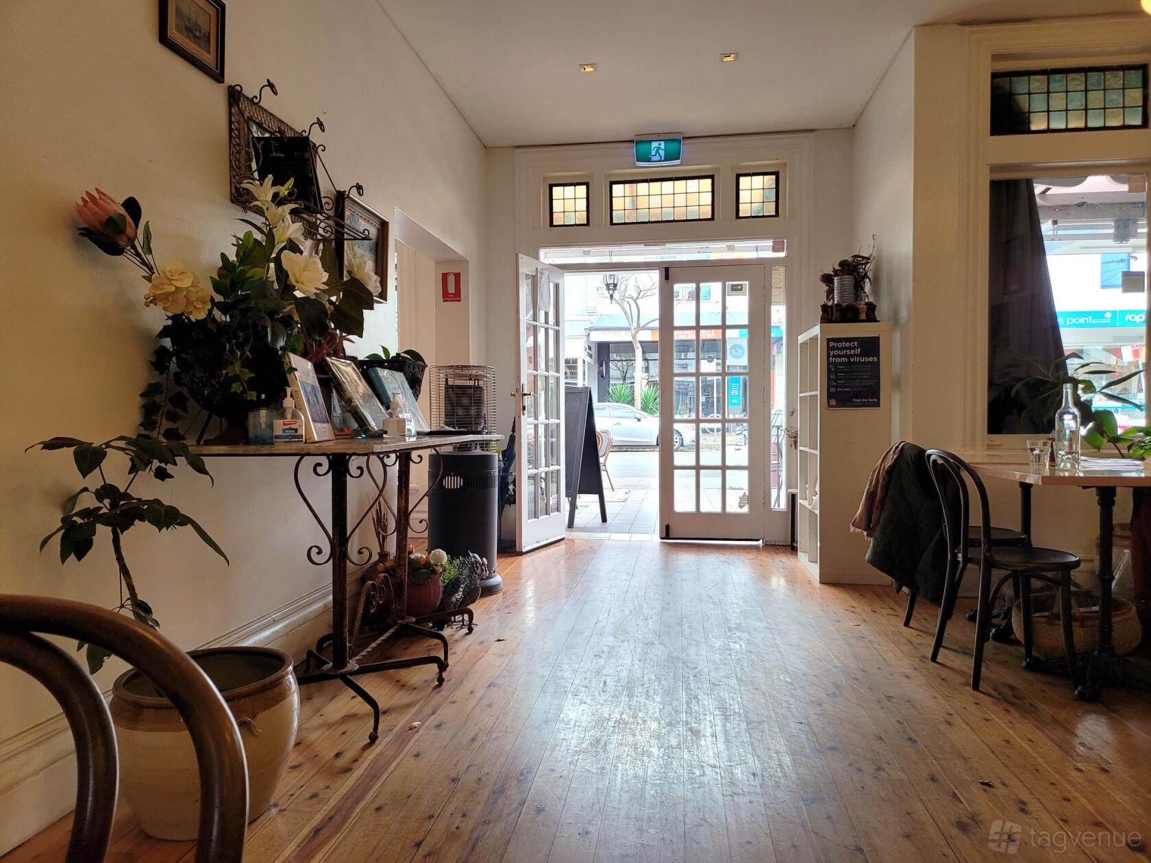 A restaurant dining room with wooden floors, potted plants, and open French doors at Billi's Cafe.