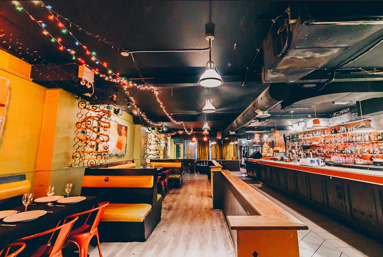 An event space in a bar with string lights, yellow booth seating, and a long bar counter at The Supermarket.