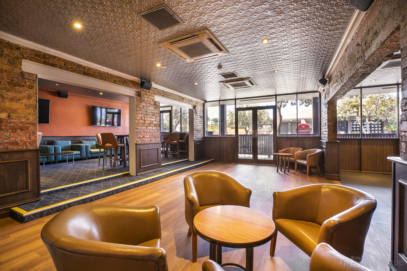 A pub lounge with exposed brick walls, brown leather chairs, wooden floors, and natural light at The Pier Hotel.