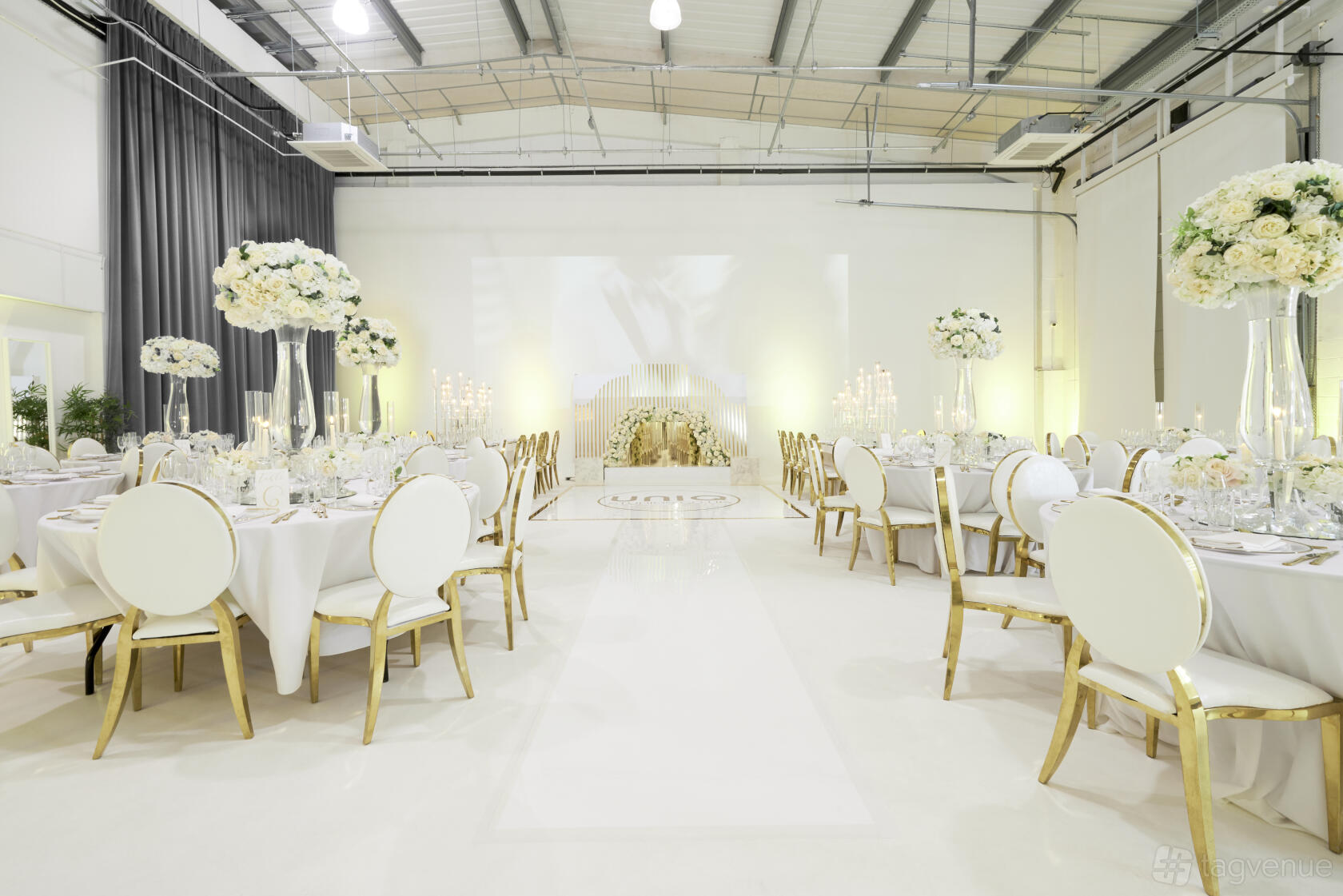 A photo studio with white walls, high ceilings, and round tables with elegant floral centerpieces at UniQ Royal Arsenal.