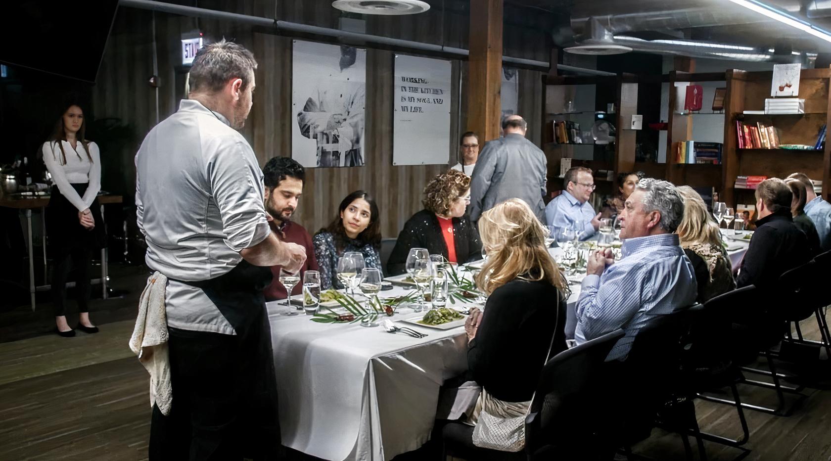 An event space in a restaurant with long tables, white linens, and exposed ductwork at Chicago Chefs' Table.