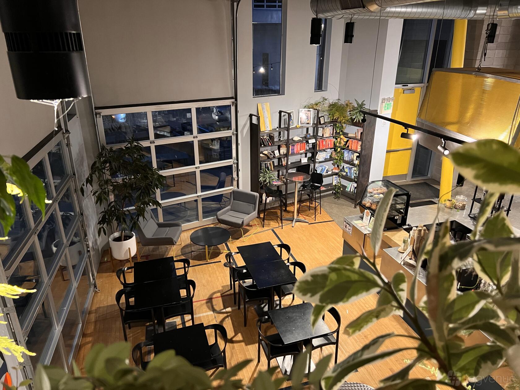 A cafe with floor-to-ceiling windows, black tables and chairs, a bookshelf, and a coffee counter at Zero Hour Cafe.