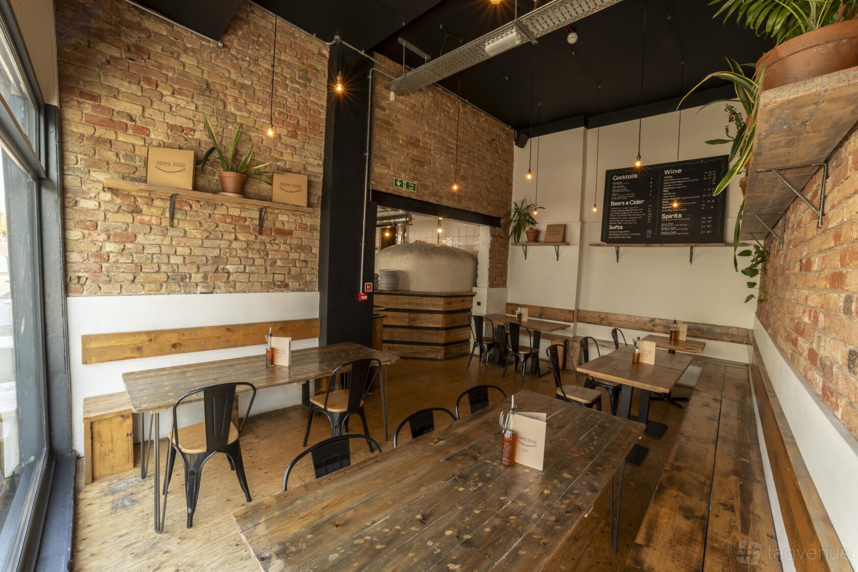 A restaurant lounge with exposed brick walls, wooden tables, and metal chairs at Mamma Dough South Norwood.