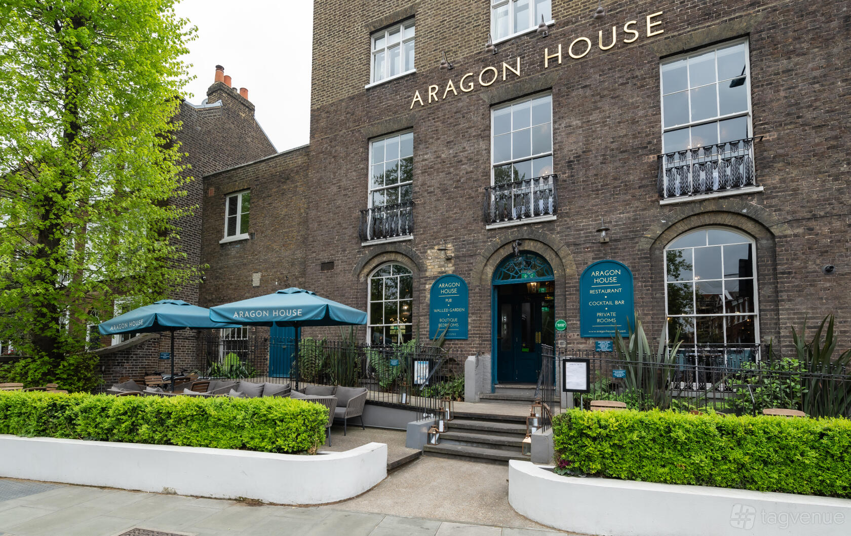 A hotel with a brick facade, arched windows, and outdoor seating with umbrellas at Aragon House.