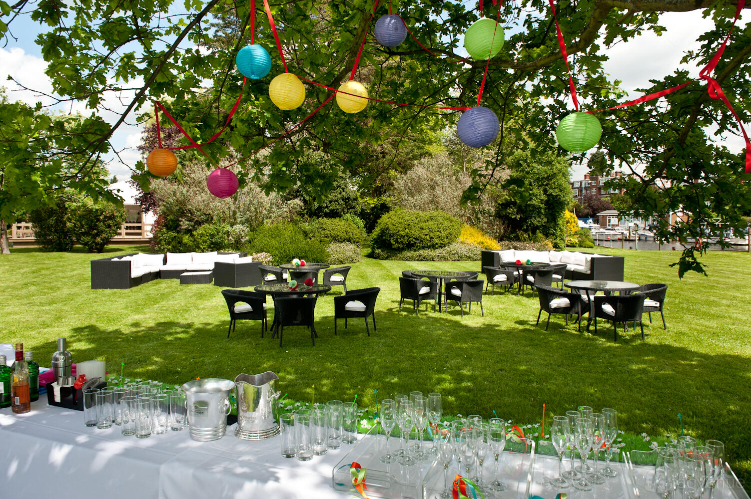 An outdoor event venue with paper lanterns, lounge seating, and a drinks station on the lawn at Ravens Ait.