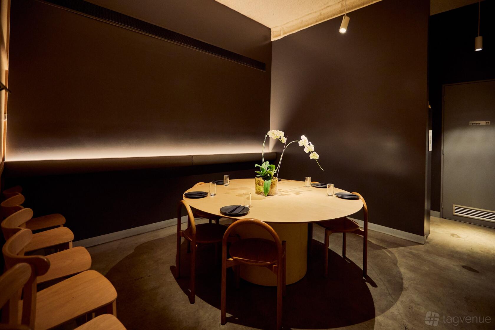 A dining room with a round wooden table, matching chairs, and potted orchids on the table at Eazy Peazy.