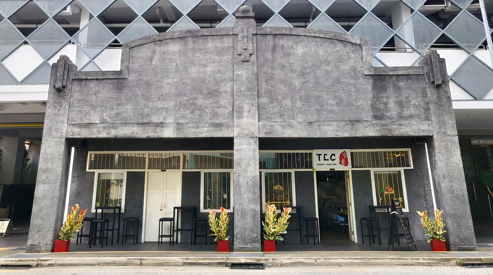 A café with a concrete facade, large windows, outdoor seating, and potted plants at the entrance at Tyrwhitt Little Cafe.