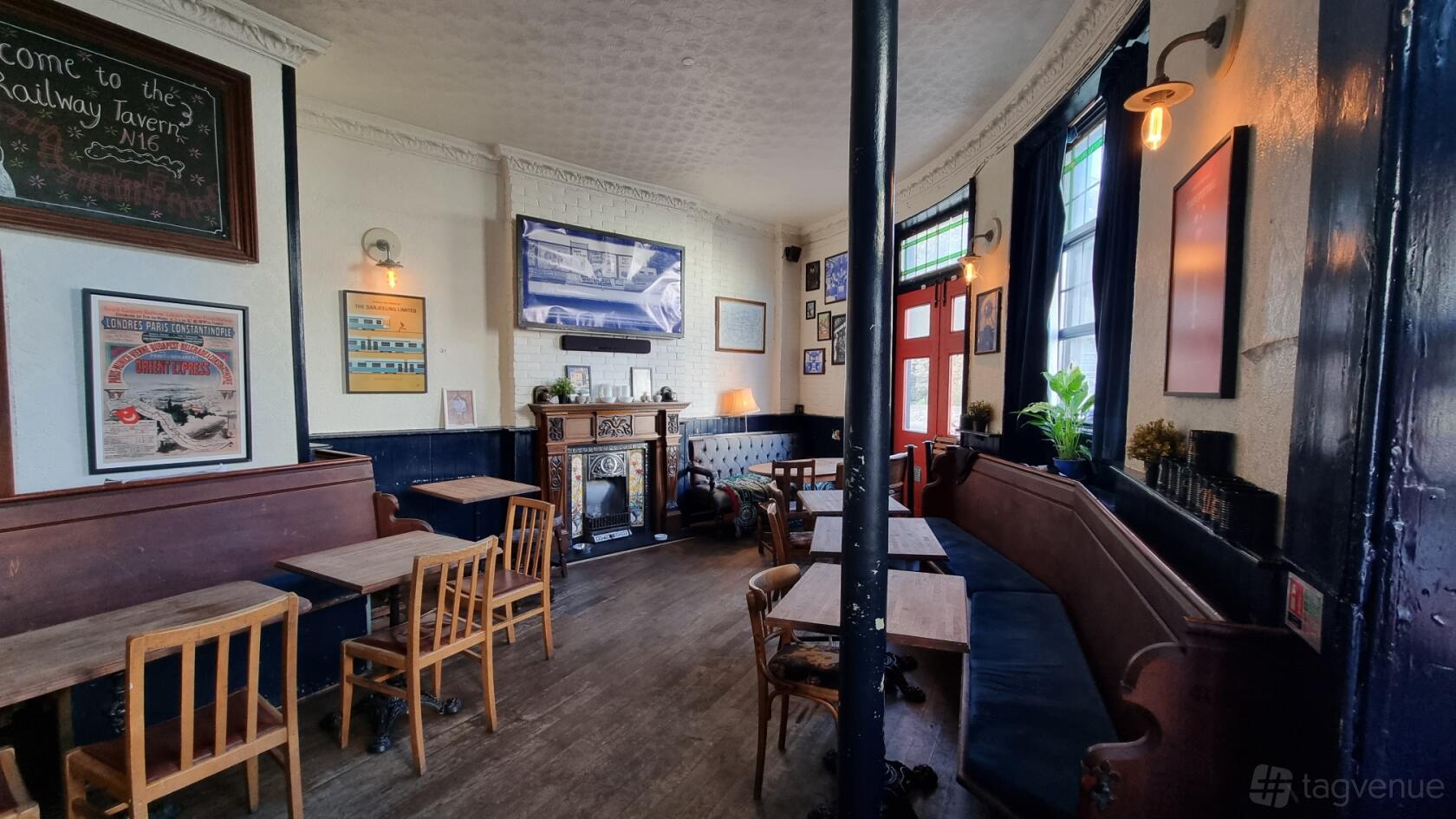 An event space in a pub with wooden tables, bentwood chairs, dark upholstered benches, and wall-mounted art at The Railway Tavern N16.