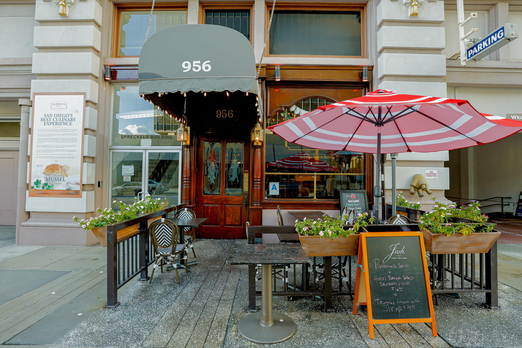 A restaurant with an outdoor patio featuring metal tables, chairs, potted plants, and a red striped umbrella at Dobson's Restaurant.