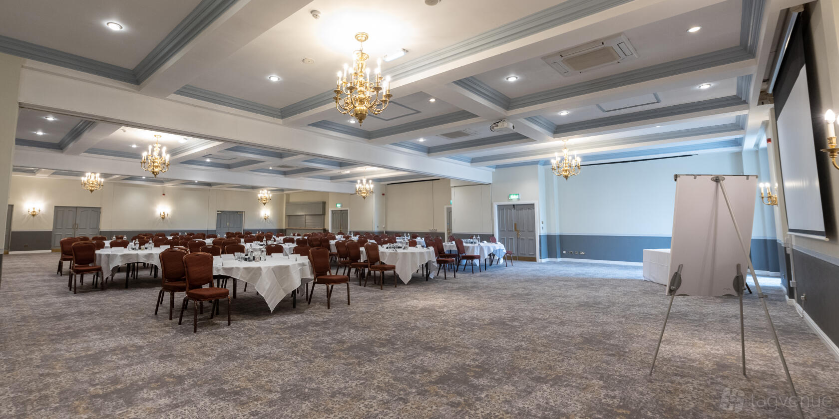 An event space with chandeliers, round tables set with white linens, and a projection screen at Mercure Tankersley Manor Hotel and Spa.