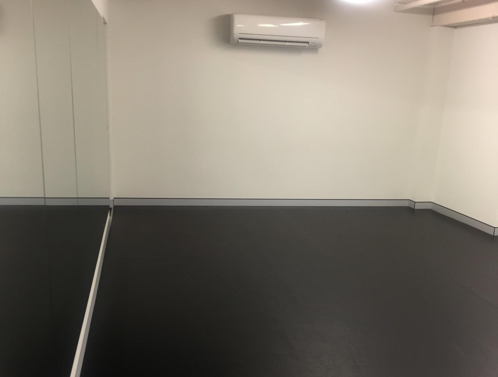 A dance studio with mirrored walls, dark flooring, and wall-mounted air conditioning at Studio at 104.