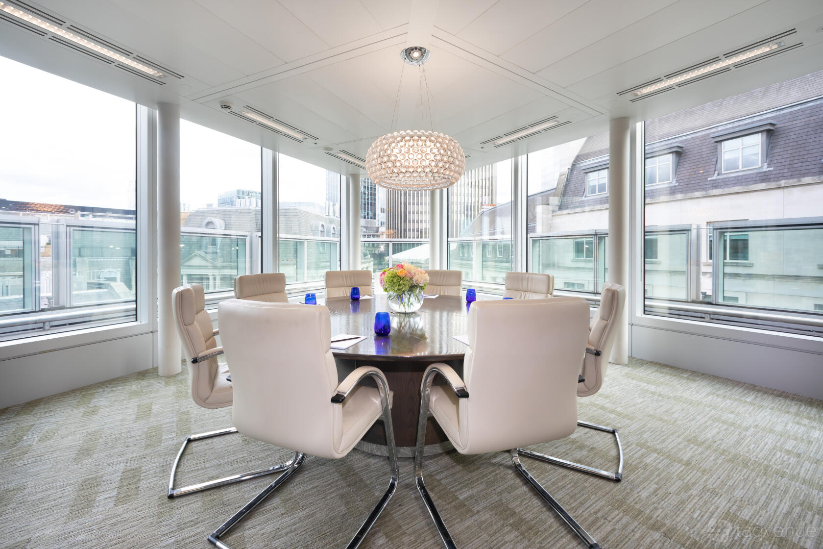 A meeting room with floor-to-ceiling windows, a round wooden table, and white chairs at Landmark: Old Broad Street, London.