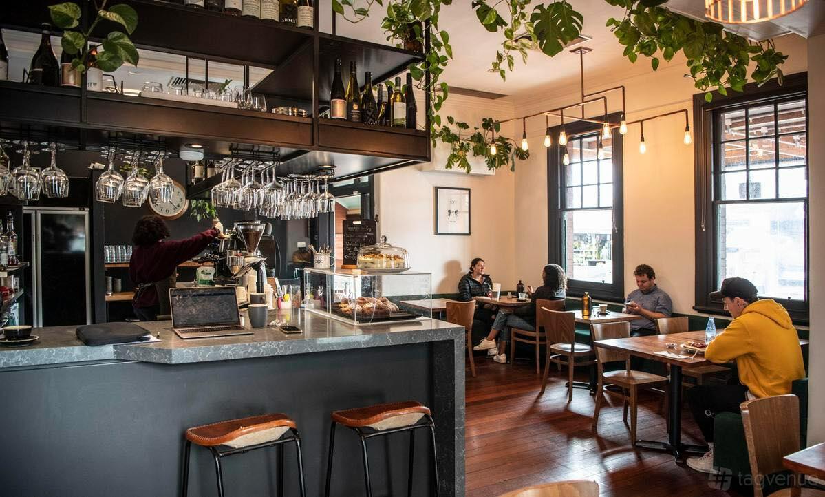 An event space in a cafe with hanging plants, large windows, wooden floors, and a counter with glassware at Sage.
