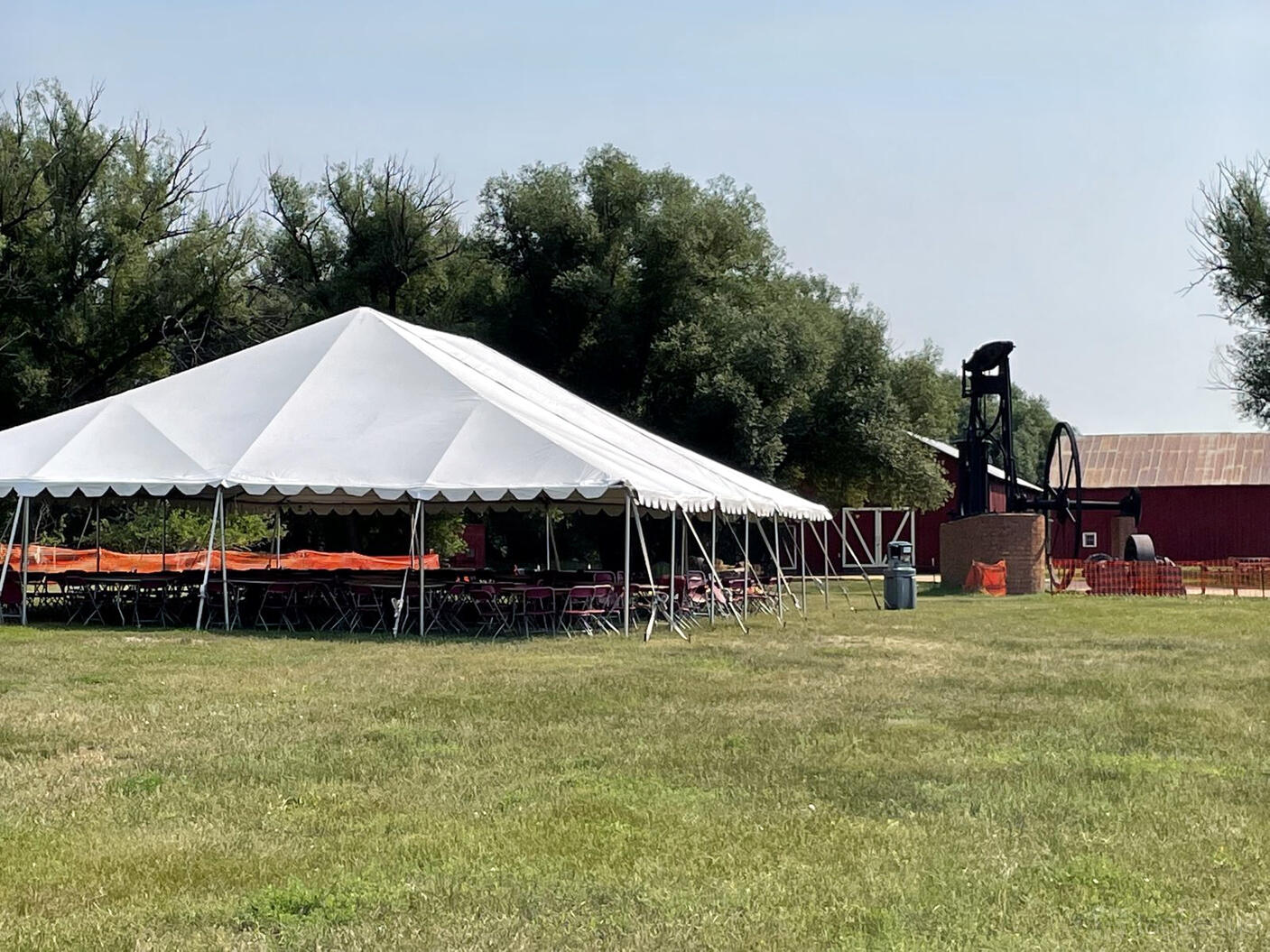 An outdoor event space with a large white tent, rows of chairs, and mining machinery at Western Museum of Mining and Industry.