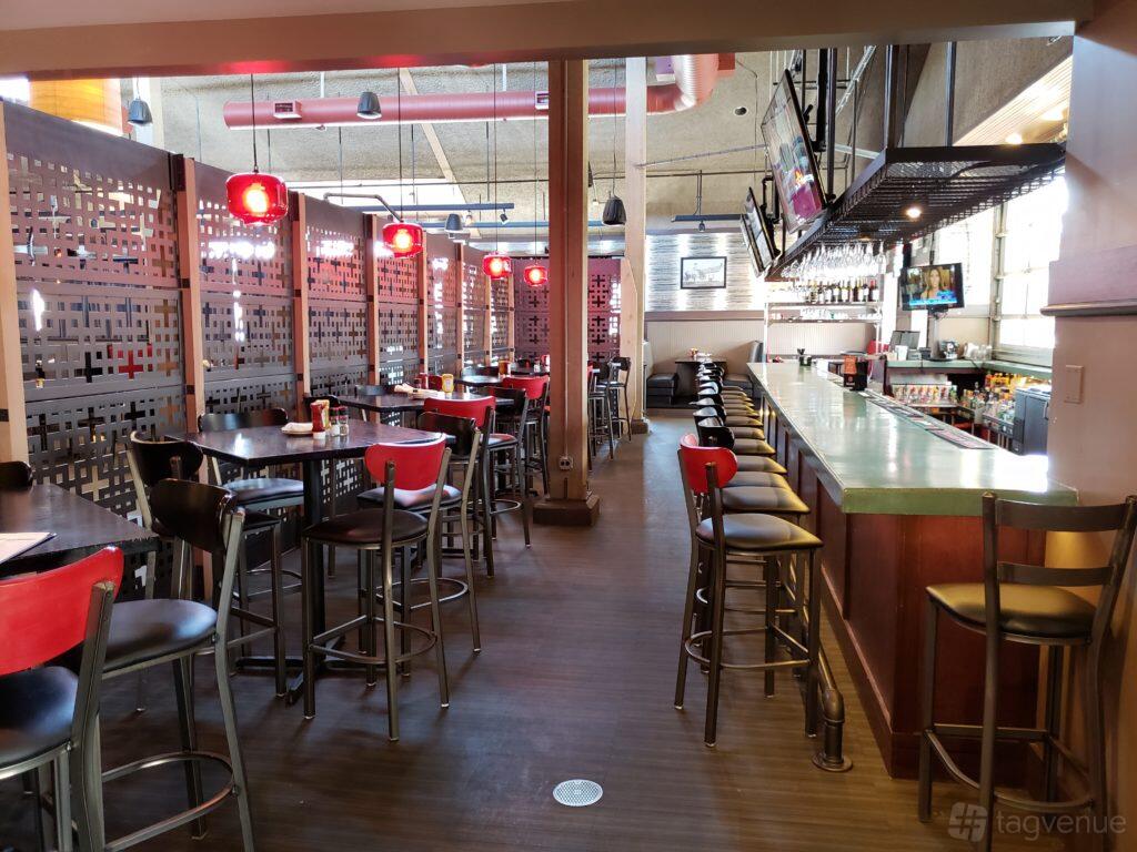 A brewery bar with high tables, red pendant lighting, and a long counter with barstools at Half Day Brewing.