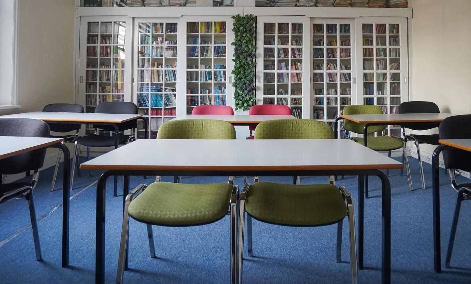 A meeting room with tables, colorful chairs, and glass-fronted bookshelves at My Meeting Space - North London College.