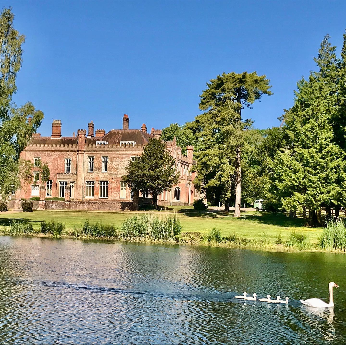 A historic hall with a brick exterior, tall chimneys, and large windows set beside a pond at Ketteringham Hall.