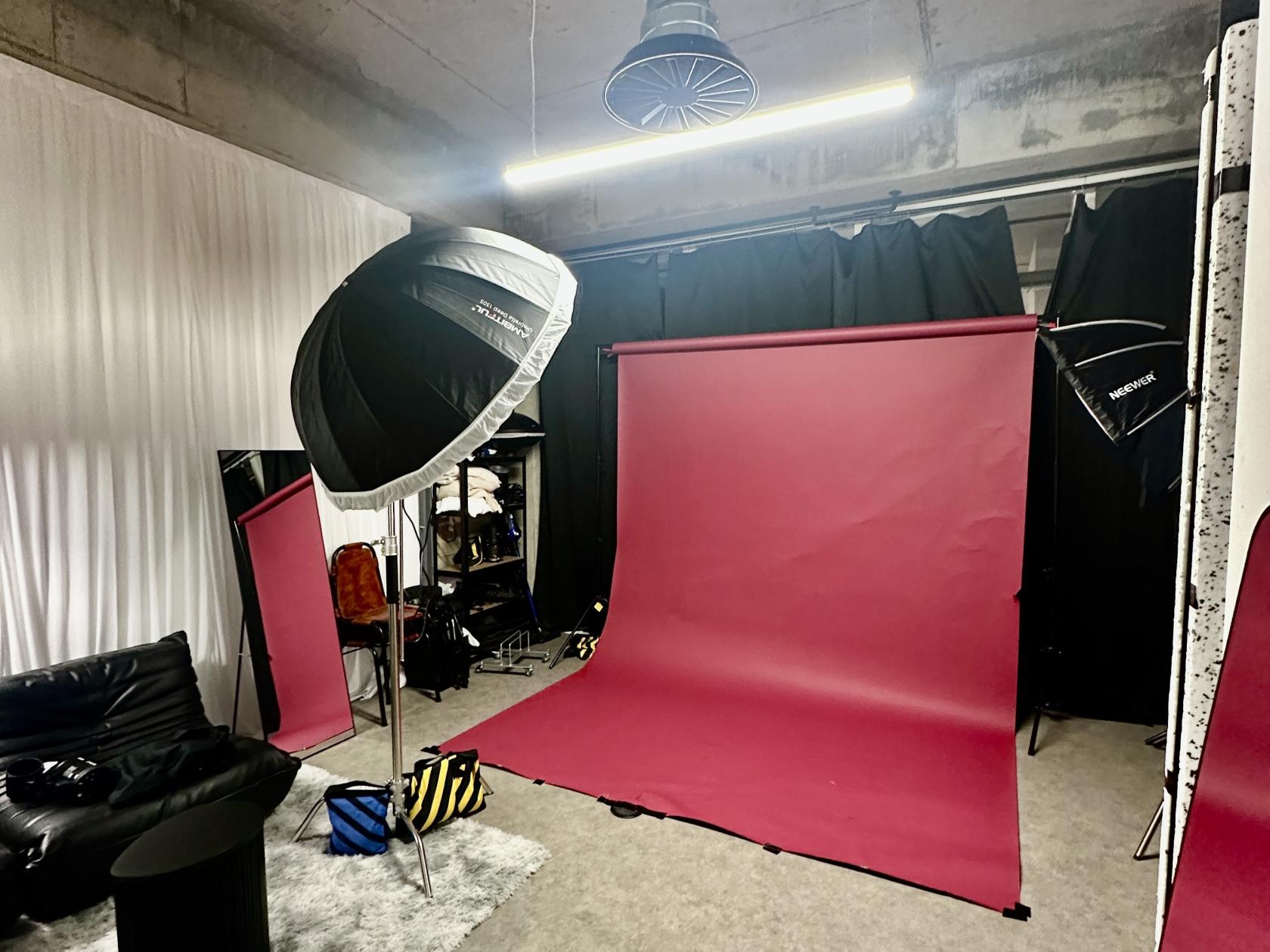 A photo studio with a red backdrop, studio lighting, black curtains, and lounge seating at Monier Studio.