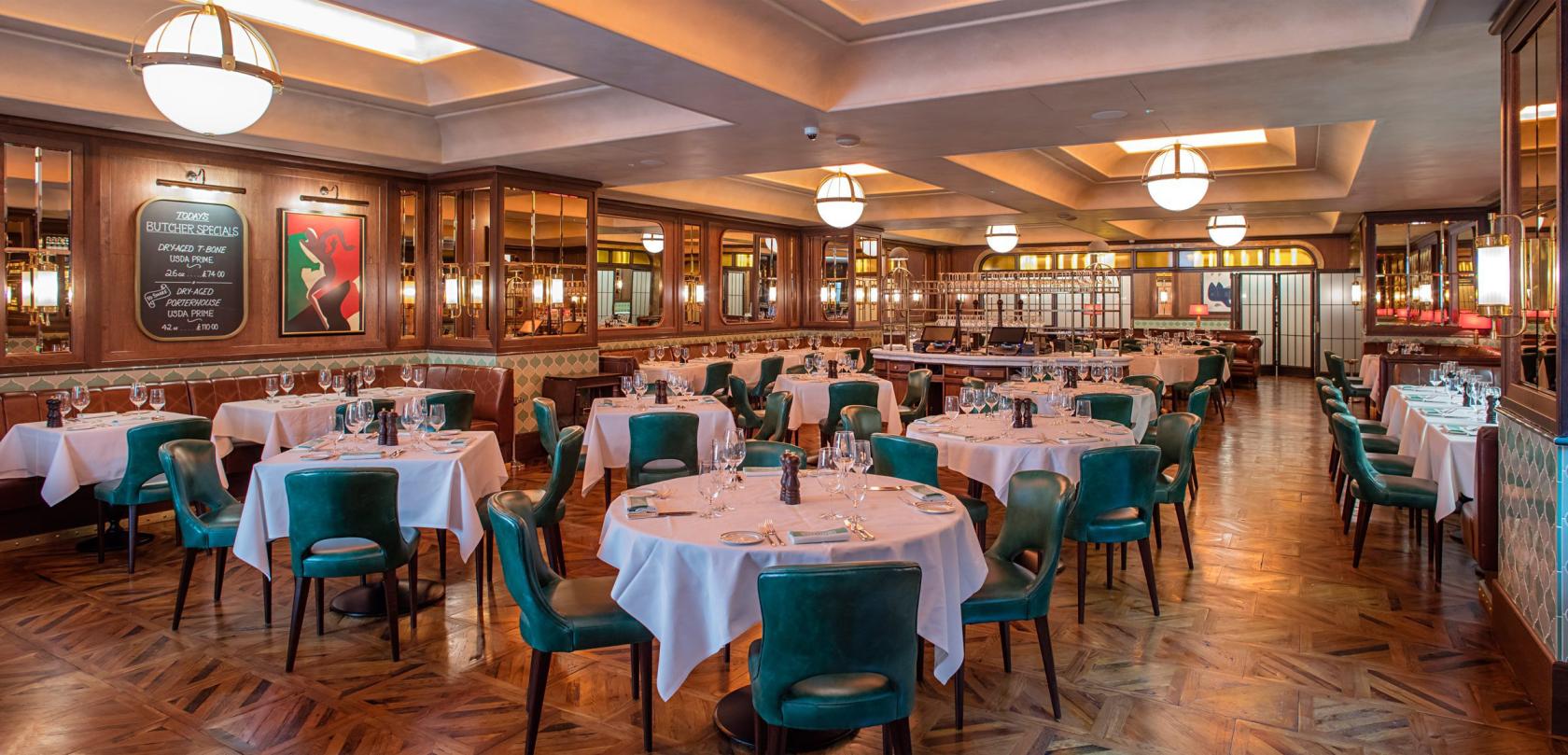 A dining room with round tables draped in white linens, green velvet chairs, and wood-paneled walls at Smith & Wollensky.