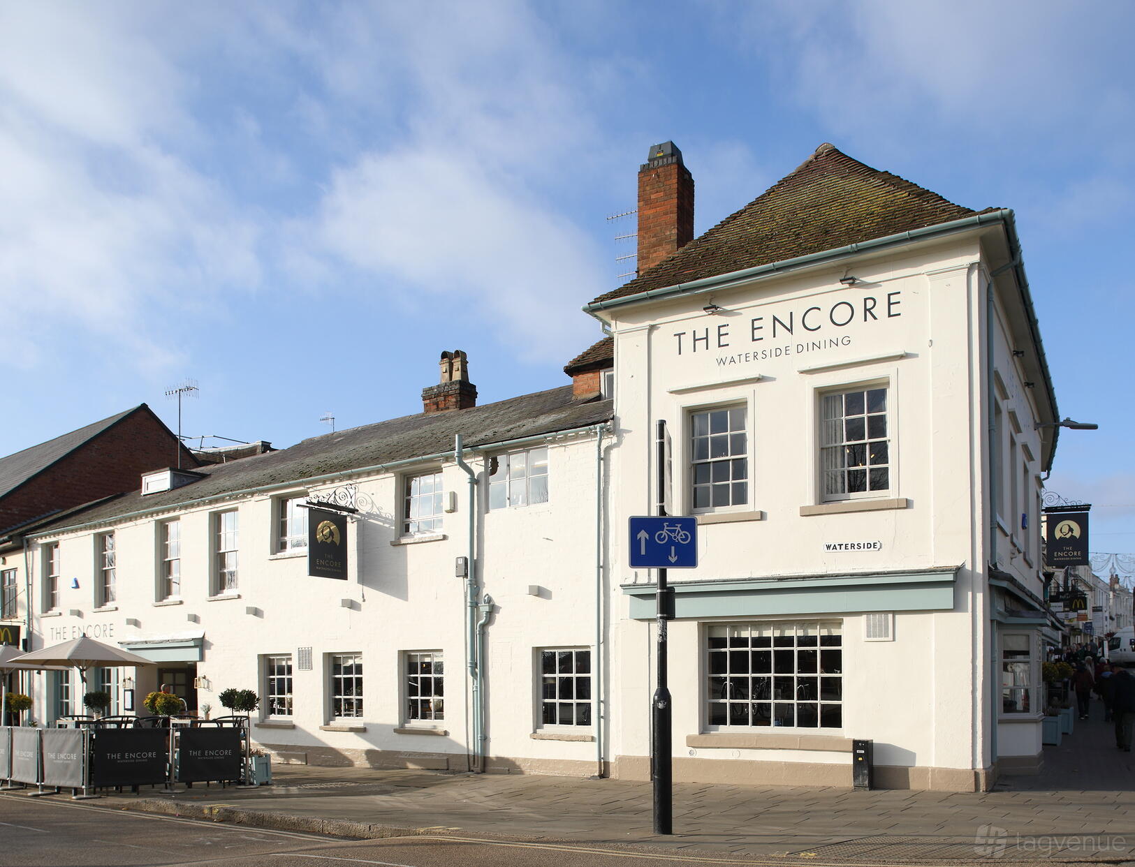 A white-painted pub with large windows, hanging signs, and traditional roof at The Encore.
