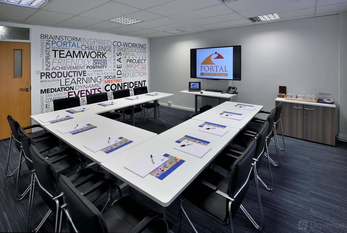 A meeting room with a U-shaped table arrangement, wall graphics, and presentation screen at Portal Business Centre Dallam Court.