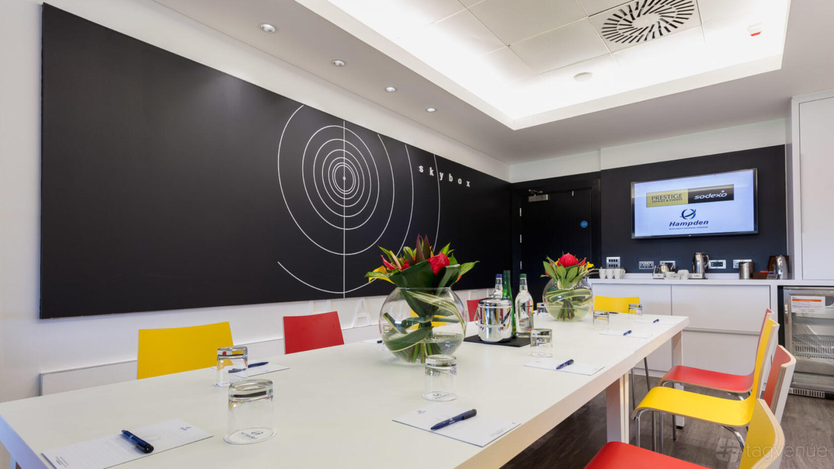 A meeting room with a long conference table, colorful chairs, and wall graphics at Hampden Park Stadium.