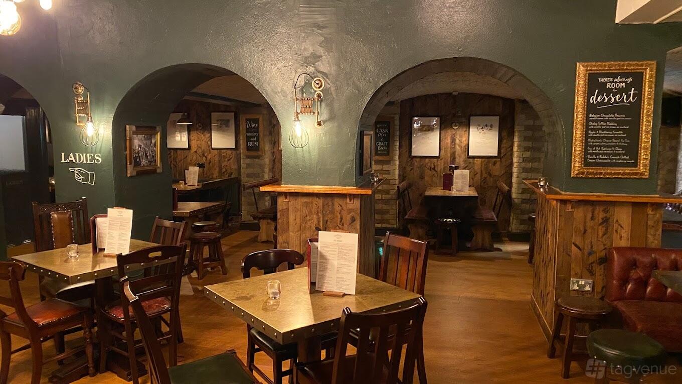 An underground pub space with arched brick alcoves, wooden tables, and menu boards at The King's Head Pub.