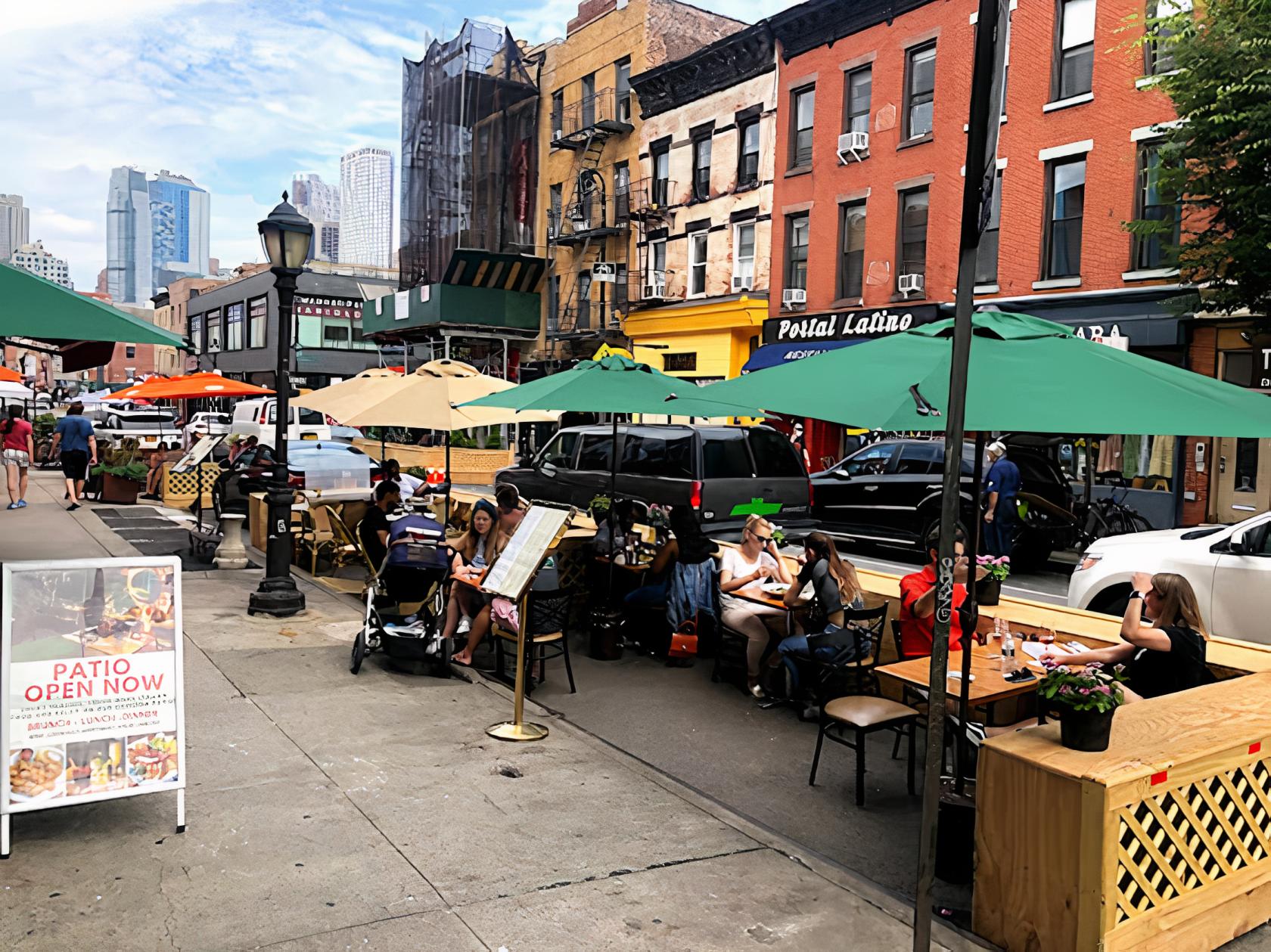 A restaurant patio with wooden tables, green umbrellas, and diners along the sidewalk at Verde on Smith.