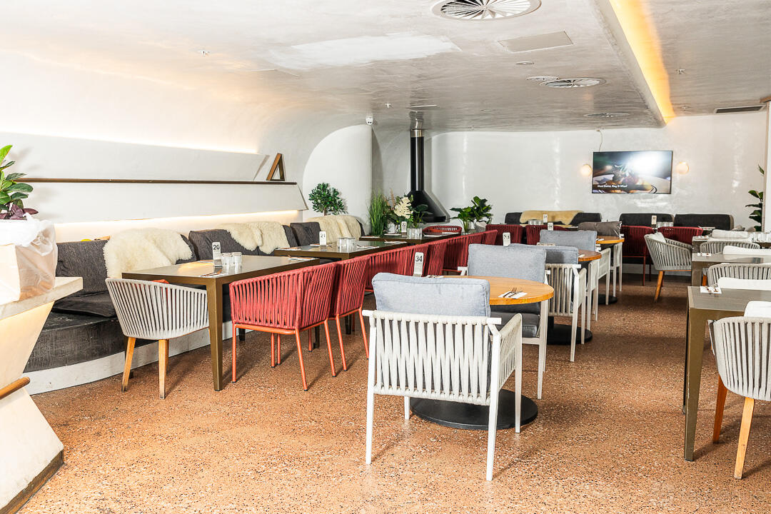 An event space with cushioned chairs, round tables, and a wall-mounted TV at Planar Restaurant.