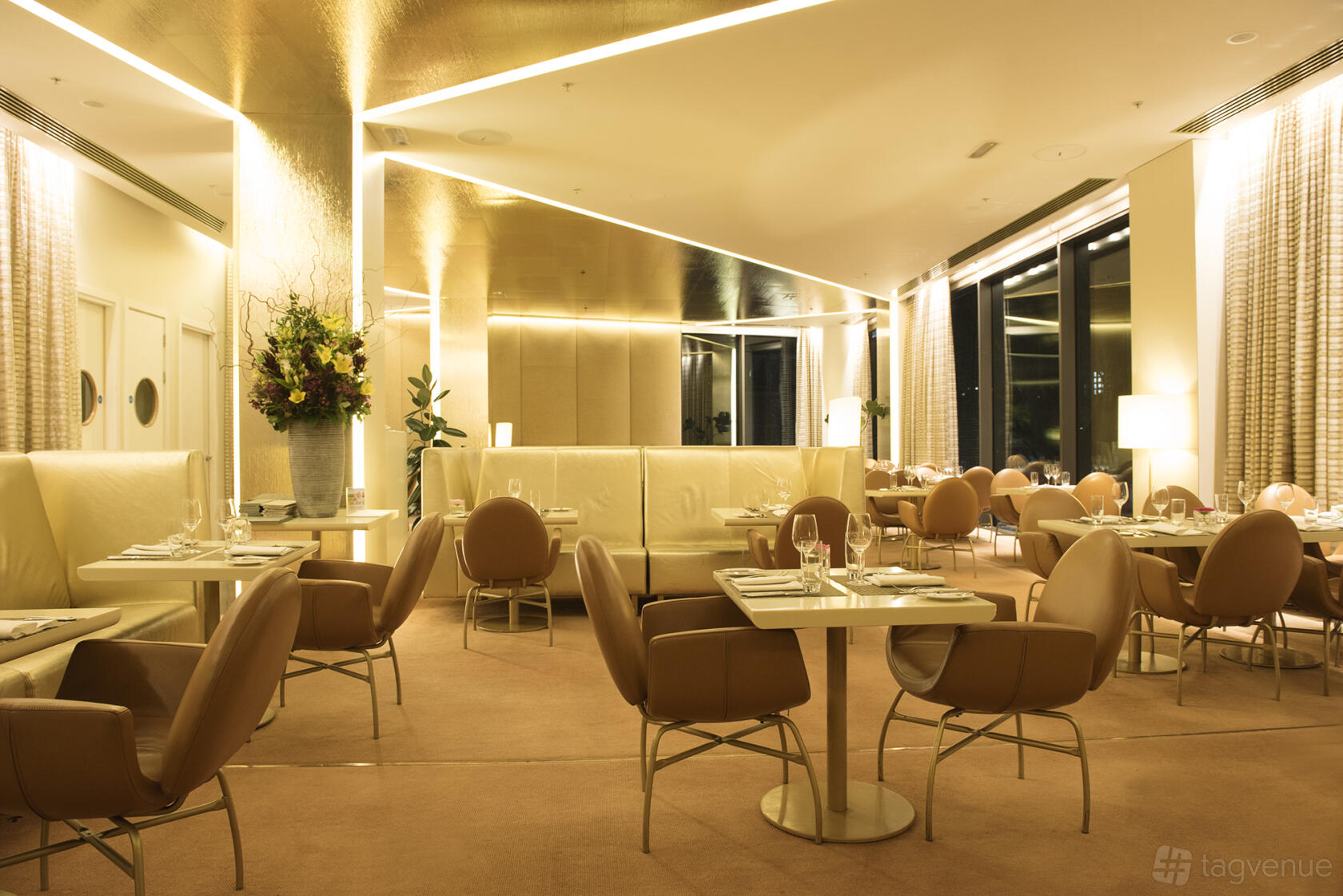A restaurant dining area with beige leather chairs, square tables, and warm lighting at Harvey Nichols Bristol.