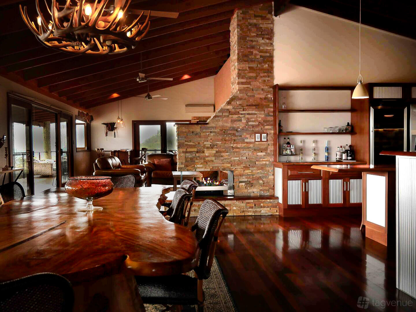 A country house with a rustic wood dining table, stone fireplace, and exposed beam ceiling at The Eagles Nest Scenic Rim.