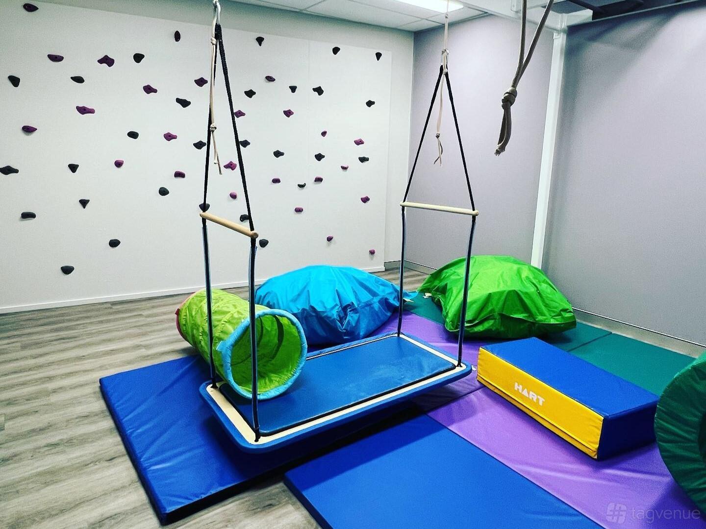 A therapy room with climbing wall grips, colorful floor mats, bean bags, and a suspended therapy swing at Inside Out Therapy.