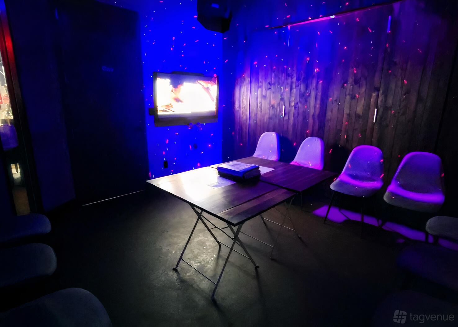 A private karaoke room with a TV screen, disco lights, wooden walls, and white chairs at Beats Karaoke Cafe.