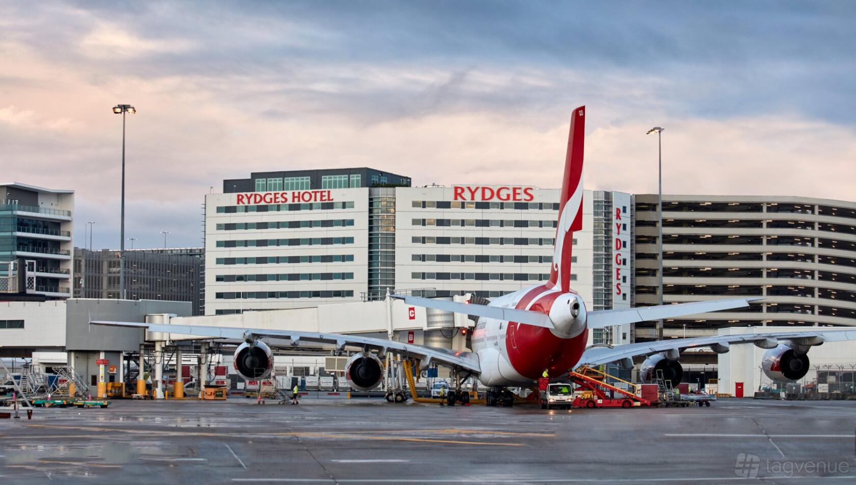 A hotel with a multi-story facade and visible red signage, adjacent to an airport runway at Rydges Sydney Airport Hotel.