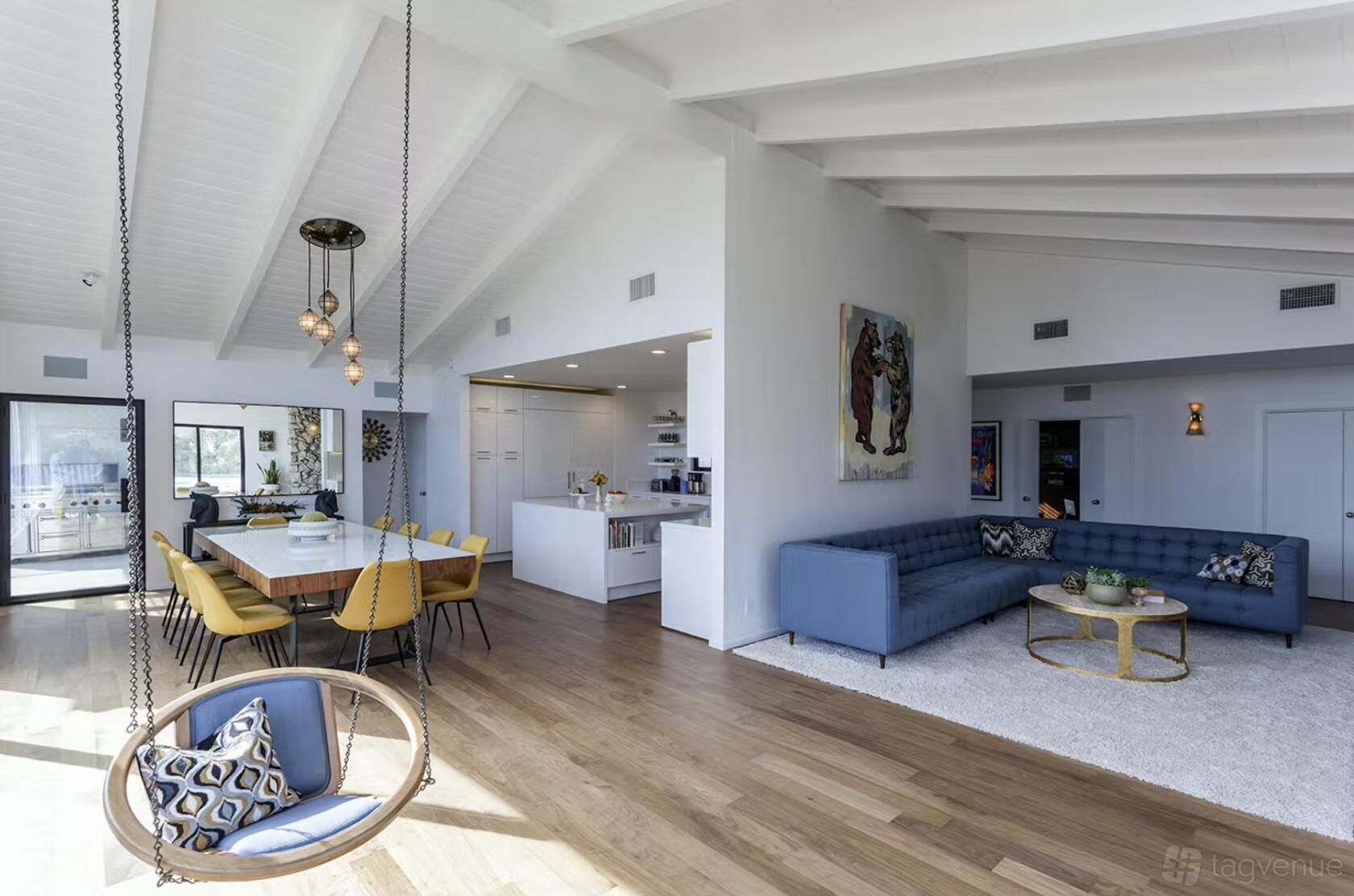 An event space in a house with vaulted ceilings, wooden floors, a hanging chair, and a blue sectional sofa at Casiano House.