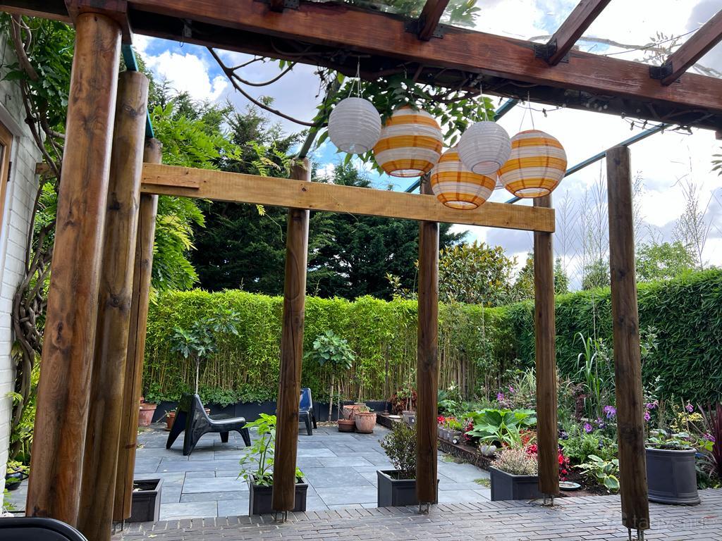 A garden with stone patio flooring, wooden pergola, paper lanterns, and potted plants at 12 Wellfield Avenue.