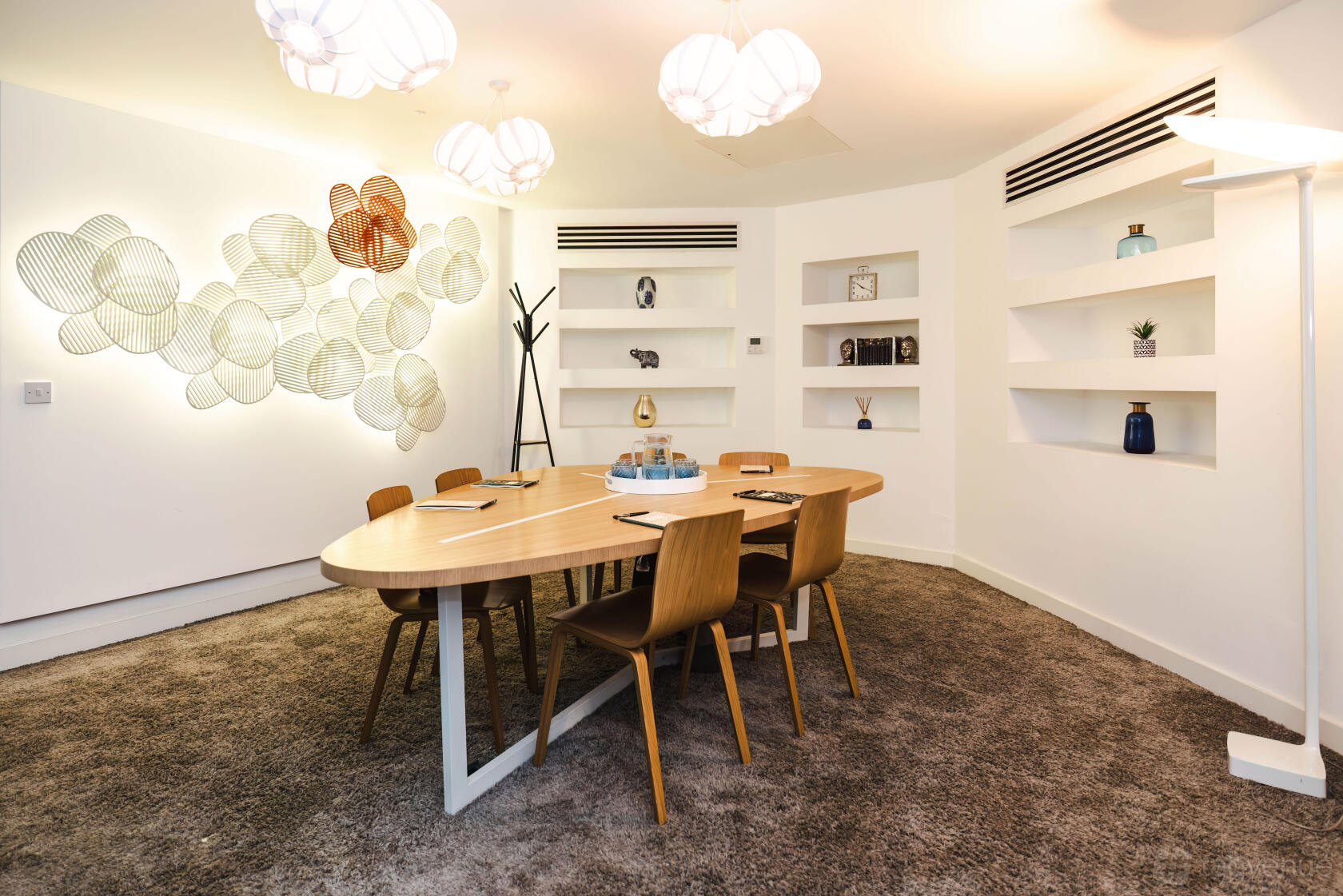 A meeting room with a wooden oval table, six chairs, decorative wall art, and built-in shelves at Golden Square.