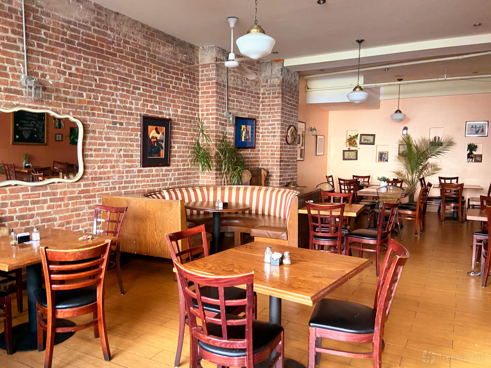 A restaurant with exposed brick walls, wooden tables, striped booth seating, and framed art at Home Sweet Harlem.