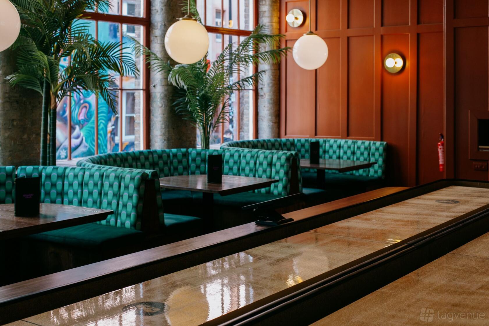 An event venue with green patterned booth seating, globe pendant lights, and large windows at Shuffle Club.