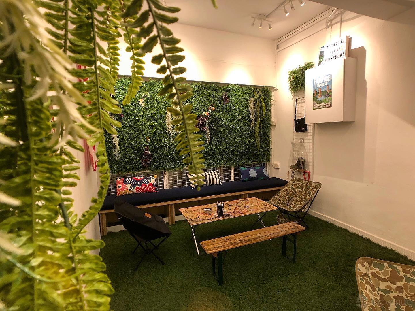 A bar with artificial grass flooring, a living plant wall, wooden tables, and colorful cushions at The Otherside.